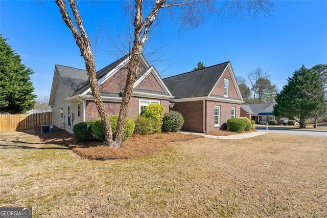 view of side of home with brick siding, central AC unit, a yard, and fence