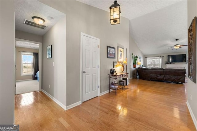 hallway featuring baseboards, wood finished floors, visible vents, and a textured ceiling