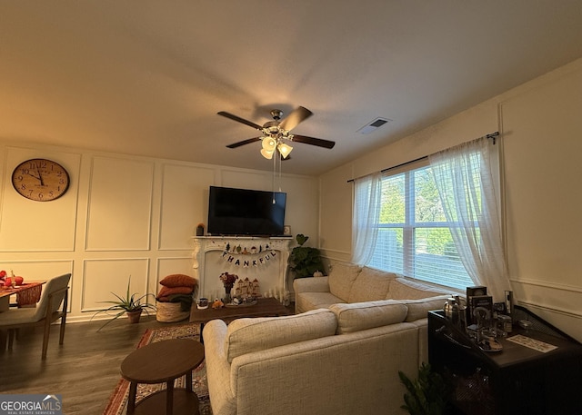 living room with a ceiling fan, a decorative wall, wood finished floors, and visible vents