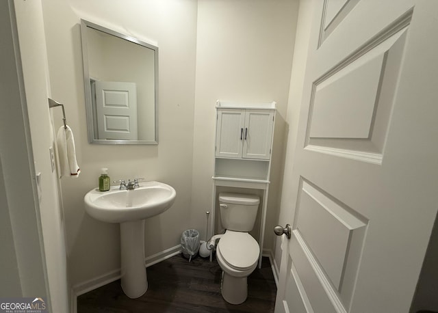 half bathroom with toilet, wood finished floors, baseboards, and a sink