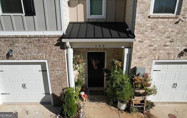 entrance to property featuring a standing seam roof, an attached garage, brick siding, and metal roof