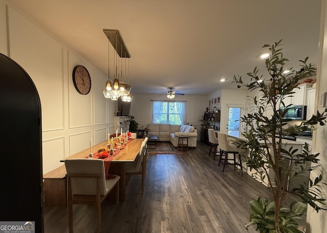 dining space featuring dark wood-style floors, a decorative wall, arched walkways, and a ceiling fan