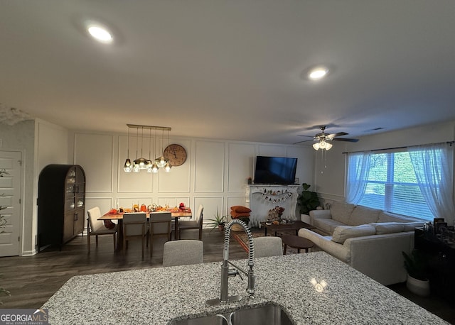 living area with dark wood-style floors, a decorative wall, visible vents, and ceiling fan