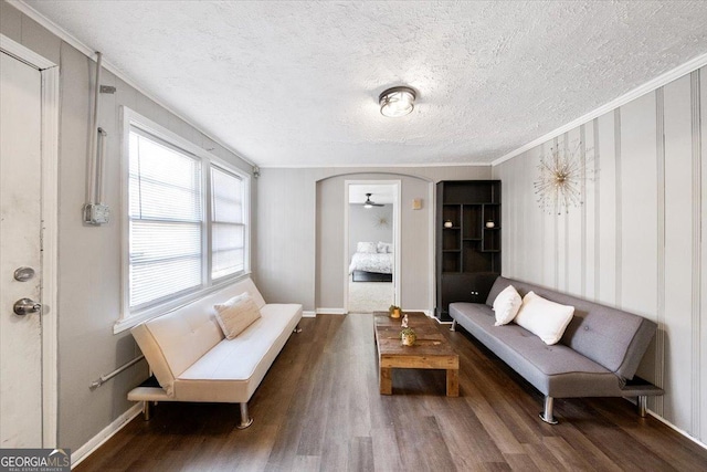 living room featuring baseboards, ornamental molding, wood finished floors, arched walkways, and a textured ceiling