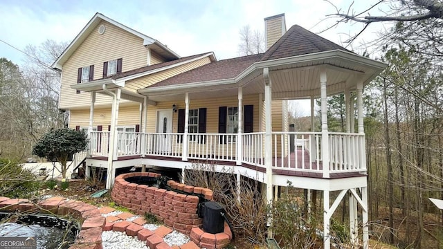 back of house featuring a porch, a chimney, and a shingled roof