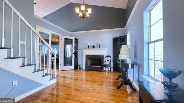 foyer with a fireplace with flush hearth, a notable chandelier, wood finished floors, stairway, and crown molding