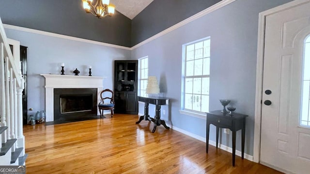 foyer entrance with wood finished floors, baseboards, an inviting chandelier, a fireplace with flush hearth, and ornamental molding