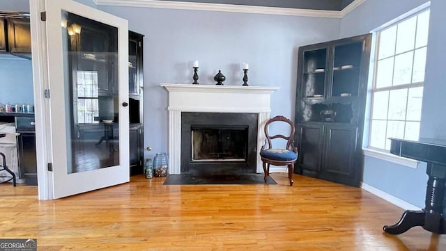 living room with a fireplace with flush hearth, ornamental molding, baseboards, and wood finished floors