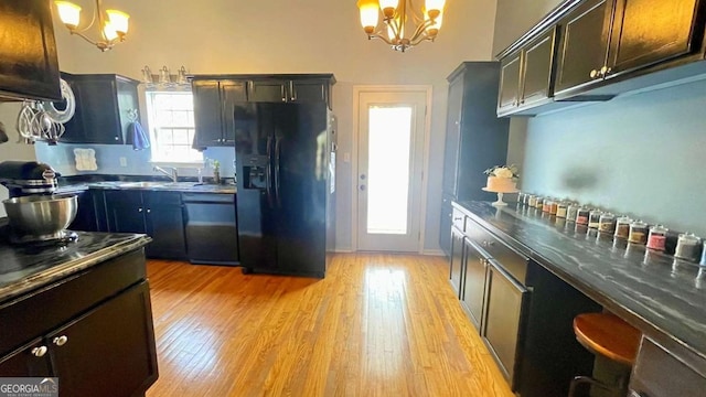 kitchen with pendant lighting, black appliances, dark countertops, light wood finished floors, and a chandelier