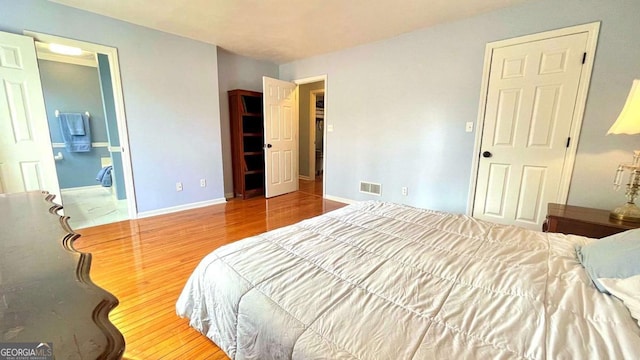 bedroom with visible vents, baseboards, ensuite bath, and wood finished floors