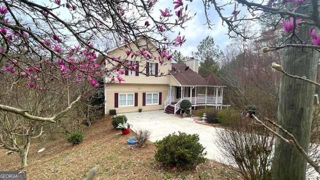 view of front of property featuring a porch, concrete driveway, and a chimney