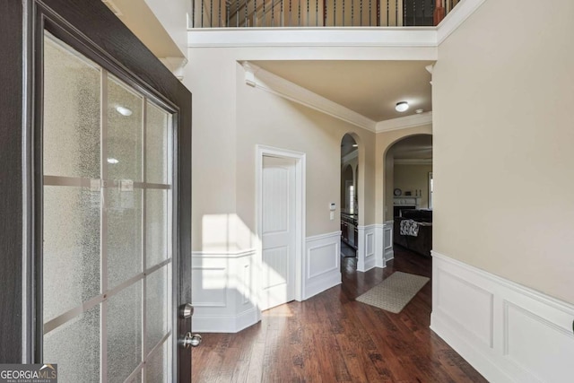 interior space featuring a wainscoted wall, arched walkways, dark wood-style flooring, crown molding, and a decorative wall