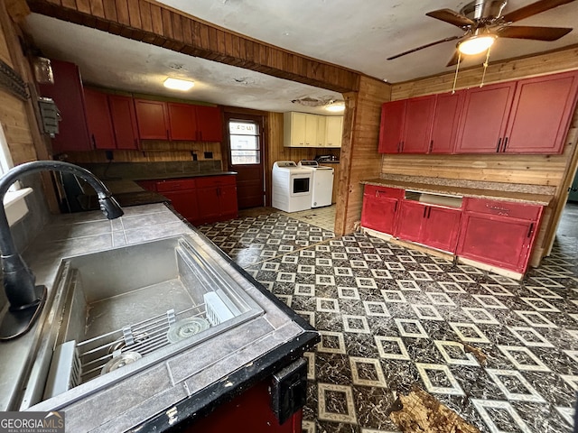 kitchen with washing machine and clothes dryer, a sink, wood walls, red cabinets, and reddish brown cabinets