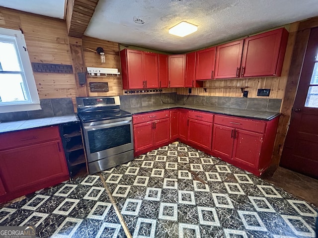 kitchen featuring red cabinetry, stainless steel electric stove, under cabinet range hood, and wooden walls