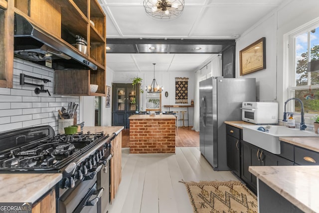 kitchen with under cabinet range hood, open shelves, a sink, an inviting chandelier, and appliances with stainless steel finishes