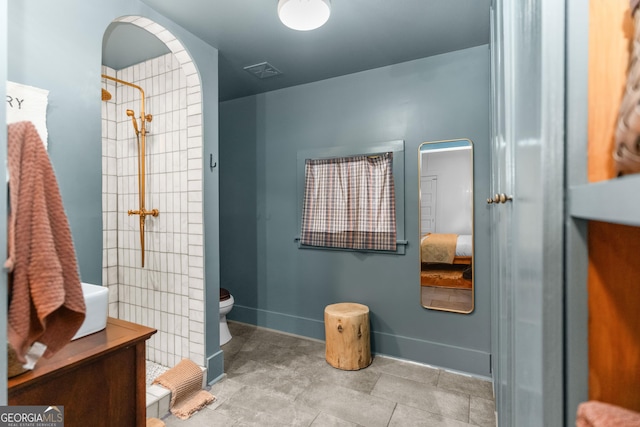 bathroom with toilet, baseboards, visible vents, and a tile shower