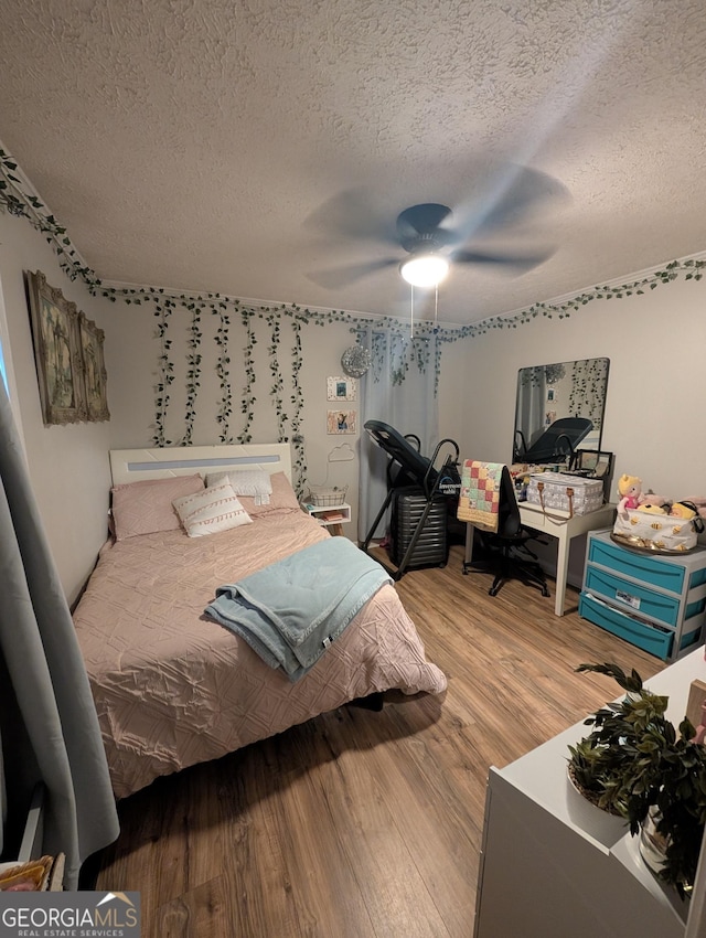 bedroom with ceiling fan, wood finished floors, and a textured ceiling