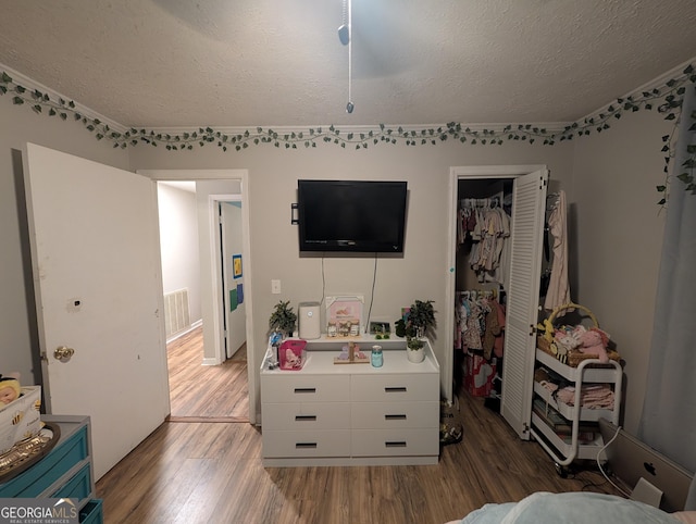 bedroom with wood finished floors, visible vents, a closet, and a textured ceiling