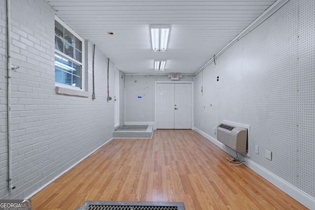 interior space with brick wall, baseboards, light wood finished floors, and a wall mounted AC