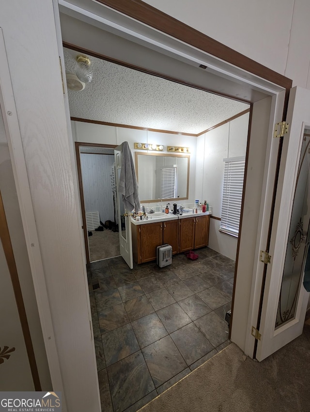 bathroom featuring double vanity, a textured ceiling, and ornamental molding