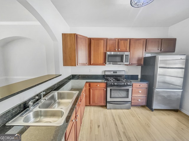 kitchen with dark countertops, light wood-type flooring, appliances with stainless steel finishes, and a sink