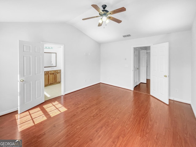 unfurnished bedroom featuring visible vents, wood finished floors, connected bathroom, baseboards, and lofted ceiling