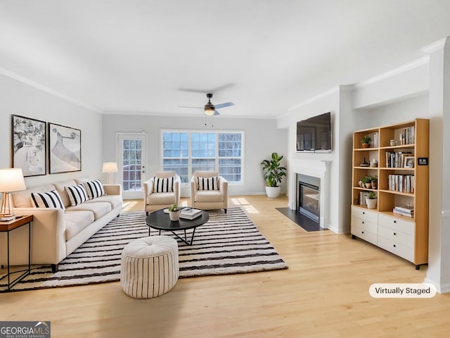 living area with a fireplace with flush hearth, ornamental molding, ceiling fan, and wood finished floors