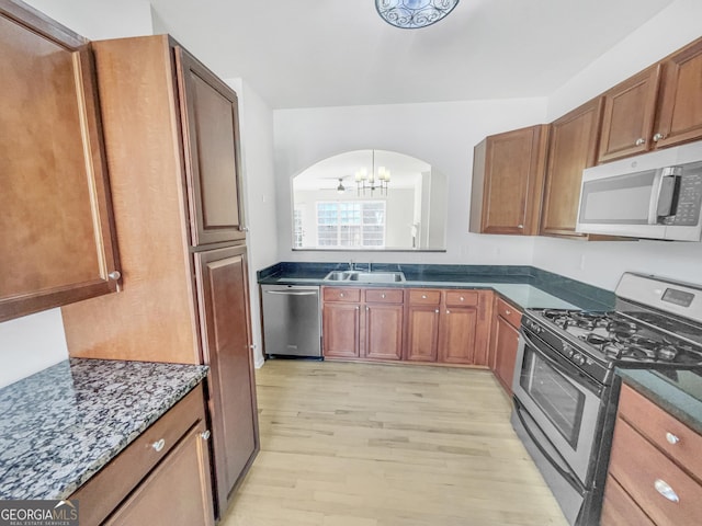 kitchen with light wood finished floors, brown cabinets, appliances with stainless steel finishes, arched walkways, and a sink