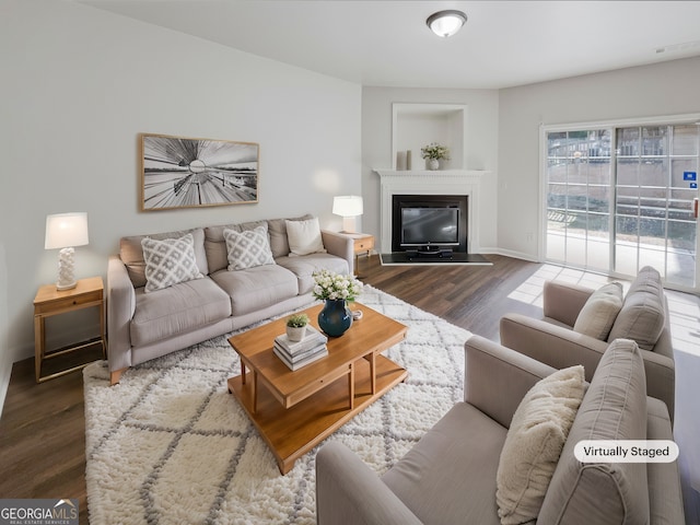 living room featuring a glass covered fireplace, visible vents, baseboards, and wood finished floors