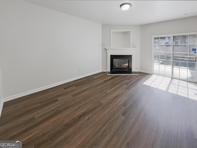 unfurnished living room with a glass covered fireplace, baseboards, and dark wood finished floors