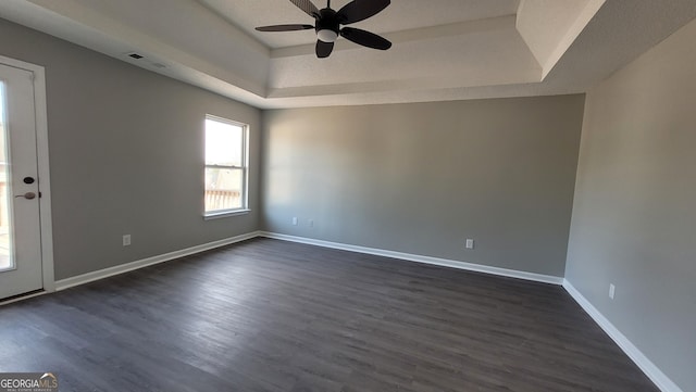 spare room featuring a tray ceiling, baseboards, dark wood-style floors, and a ceiling fan