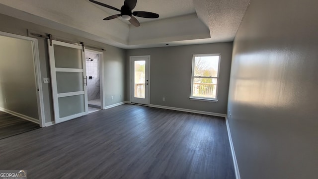 spare room with baseboards, a tray ceiling, a barn door, a ceiling fan, and dark wood-style flooring