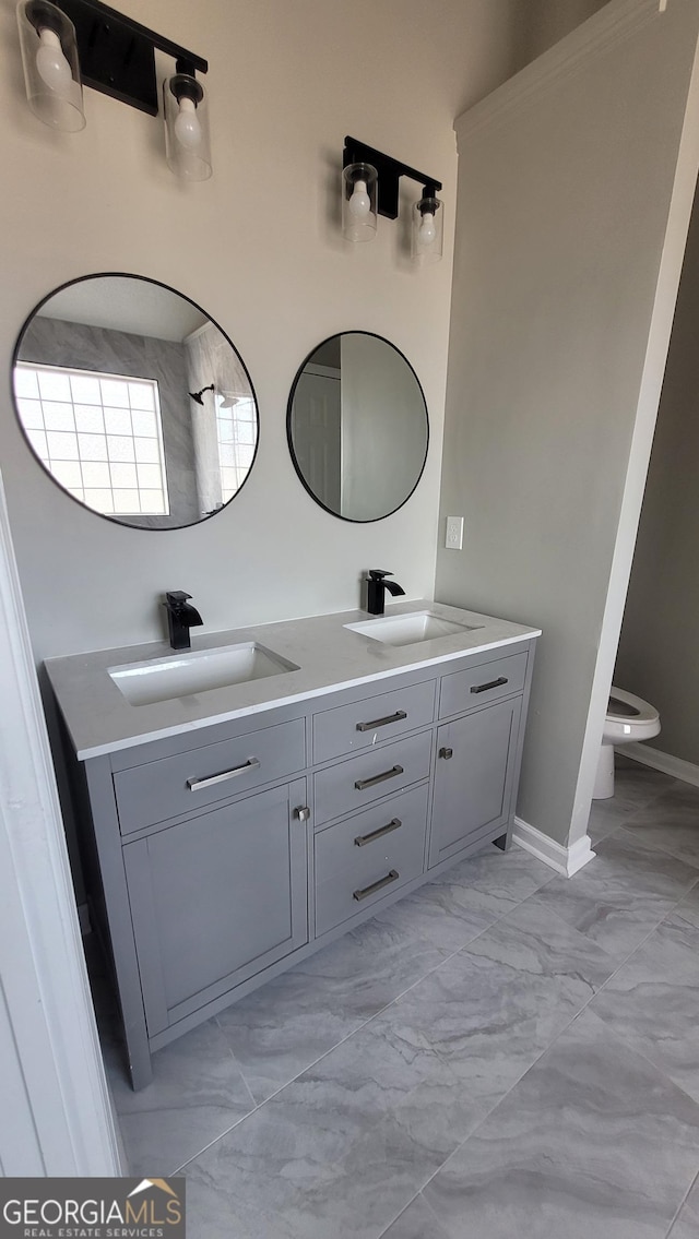 bathroom featuring double vanity, marble finish floor, toilet, and a sink