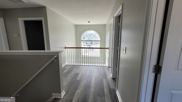 hallway with baseboards, an inviting chandelier, dark wood-type flooring, a textured ceiling, and an upstairs landing