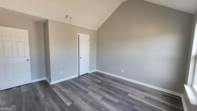 unfurnished bedroom with dark wood-style floors, visible vents, baseboards, and vaulted ceiling