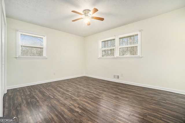 empty room featuring visible vents, a ceiling fan, a textured ceiling, dark wood finished floors, and baseboards