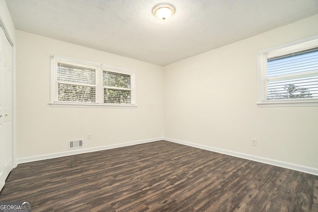 unfurnished bedroom with visible vents, dark wood-type flooring, a textured ceiling, a closet, and baseboards