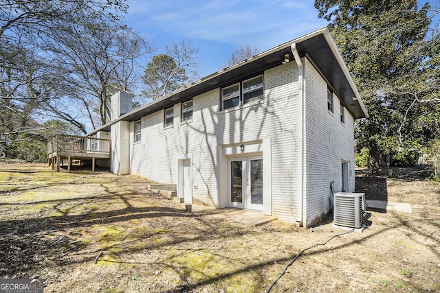 back of house with central AC unit, a chimney, french doors, a deck, and brick siding