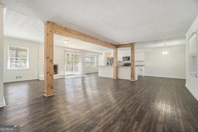 unfurnished living room with dark wood-style floors, visible vents, a fireplace, and a wealth of natural light