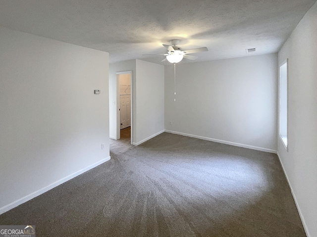 empty room featuring visible vents, a textured ceiling, dark carpet, baseboards, and ceiling fan