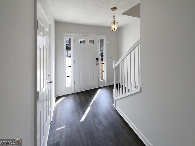 entryway featuring a textured ceiling, stairs, dark wood-type flooring, and baseboards