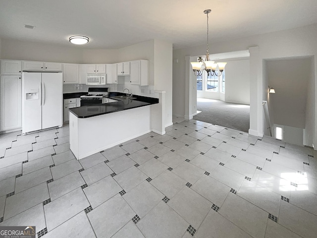 kitchen with dark countertops, a chandelier, a peninsula, white appliances, and white cabinetry