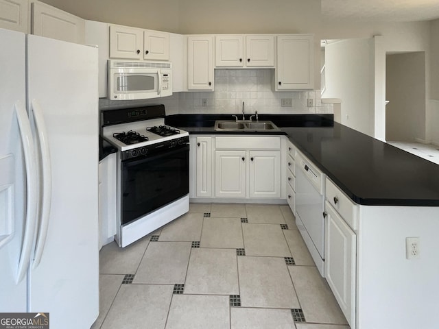 kitchen featuring white appliances, dark countertops, a peninsula, and a sink