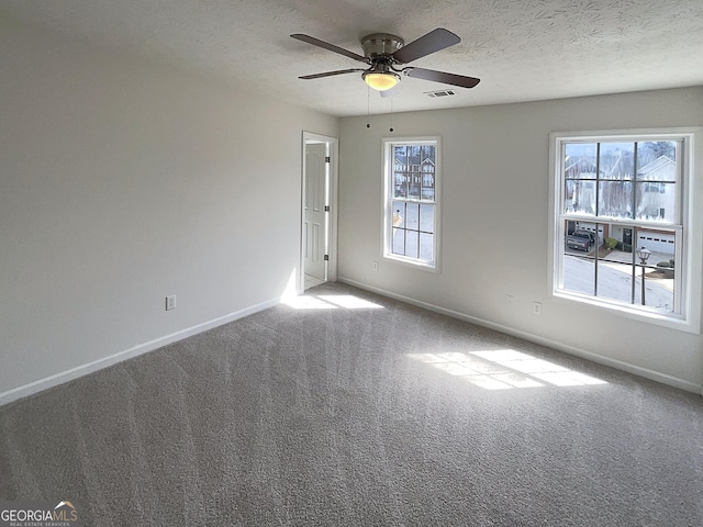 carpeted empty room featuring visible vents, a textured ceiling, and a healthy amount of sunlight