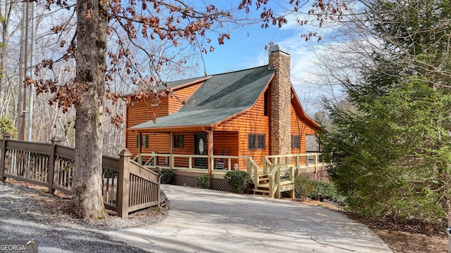 view of front of house with log veneer siding, roof with shingles, driveway, a porch, and a chimney