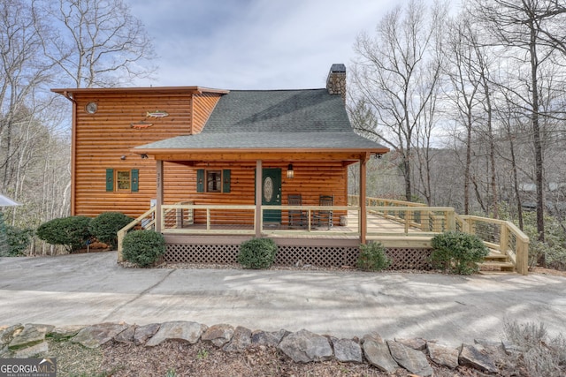 back of house featuring log veneer siding, roof with shingles, covered porch, and a chimney