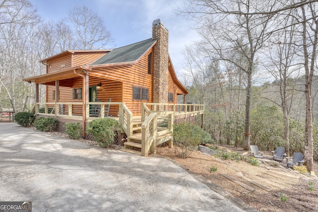 view of side of property featuring log veneer siding, a porch, and a chimney