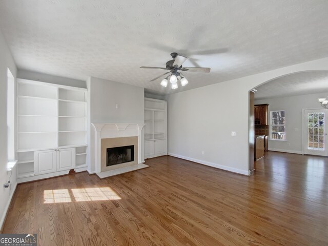 unfurnished living room with wood finished floors, a fireplace, arched walkways, and a textured ceiling