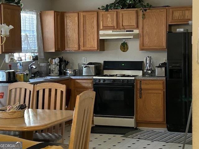 kitchen featuring under cabinet range hood, gas stove, and black refrigerator with ice dispenser