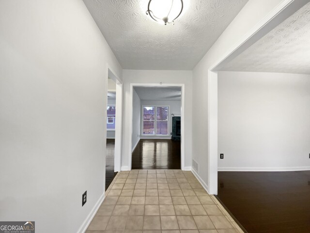 hall with light tile patterned floors, baseboards, and a textured ceiling